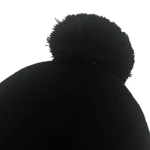 Dettaglio del berretto in maglia nera che mostra il pompon morbido e la trama a costine