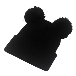 Dettaglio del berretto in maglia nera con due pompon in morbida ecopelliccia sulla cima