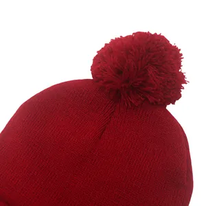 Dettaglio di un berretto in maglia bordeaux con trama e grande pompon in filato
