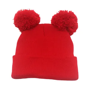 Dettaglio macro del berretto in maglia rossa con doppio pompon e trama a coste invernali