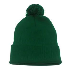 Dettaglio del berretto in maglia verde scuro con un grande pompon e trama spessa