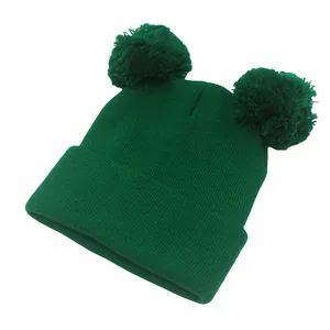 Dettaglio del berretto in maglia verde scuro con doppi pompon e bordo con risvolto