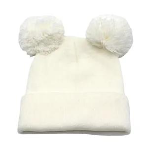 Dettaglio di un berretto in maglia bianco con doppi pompon soffici e trama a coste