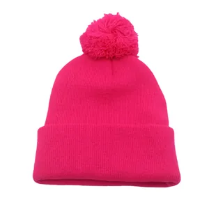 Dettaglio della maglia di un berretto fucsia con pompon soffice e risvolto alto