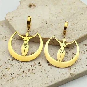 Close-up of golden moon goddess earrings with spiral totem on beige stone background