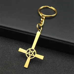 Detail of a golden metal inverted cross keychain with pentagram cutout on black texture