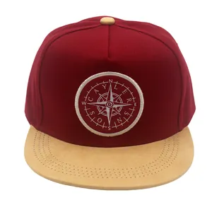 Detail of burgundy snapback hat with khaki suede brim and compass embroidery patch