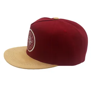 Detail of burgundy snapback hat with khaki brim and compass embroidery on white background