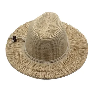 Close-up of beige straw sun hat featuring fringe brim and decorative wooden beads