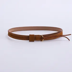 Détail d'un bandeau de chapeau en daim marron avec boucle dorée en O et finitions glands