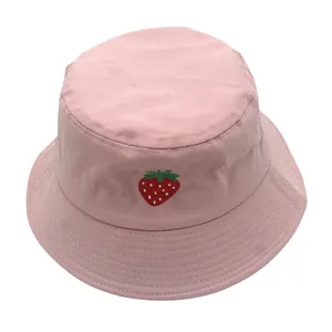 Dettaglio del ricamo a fragola su un cappello a secchiello in cotone rosa con cuciture