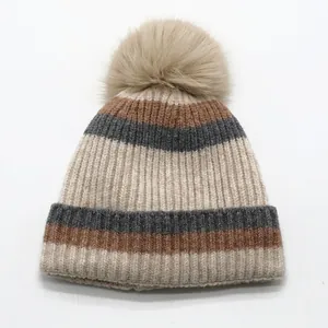 Close-up of fluffy faux fur pom-pom and thick ribbed knit texture on striped winter hat