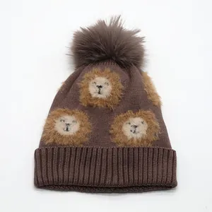 Detail of brown knitted child hat featuring cute lion patterns and a fluffy pom-pom top
