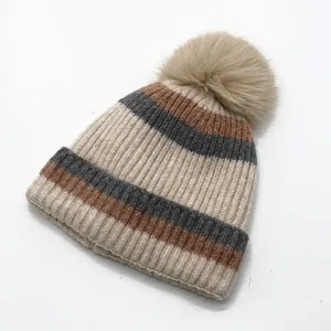 Close-up of striped knit beanie featuring thick ribbing and fluffy faux fur pompom detail