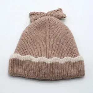 Détail d'un bonnet en maille pour enfant avec nœud et motif ondulé en beige et brun