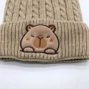 Detail of cable knit pattern and cute capybara plush patch on warm winter beanie hat