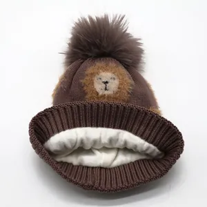 Deep brown knitted baby lion hat with a large faux fur pompom and warm fleece lining