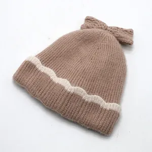 Détail du bonnet en tricot marron avec rayures ondulées blanches et un grand nœud