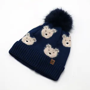 Detail of navy knit beanie with fluffy pom pom, bear pattern and brown leather label