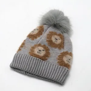 Close-up of grey knit hat featuring cartoon lion patterns and a large fluffy faux fur pompom