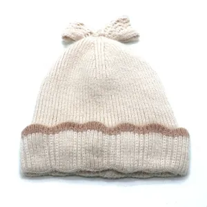Détail du bonnet en tricot crème avec motifs ondulés marrons et grand nœud décoratif