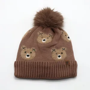 Detailed knit texture of a brown winter hat with teddy bear patterns and faux fur pompom