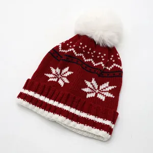 Détail d'un bonnet en tricot rouge foncé avec un pompon blanc doux et des motifs de flocons