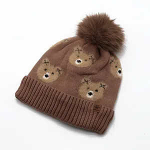 Detail of knitted bear pattern and soft faux fur pompom on brown winter beanie hat