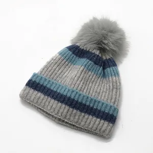 Close-up of striped knit hat featuring a large grey faux fur pom pom and warm fleece lining