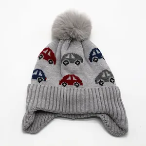 Detail of grey knitted kids hat with car jacquard patterns and fluffy pompom