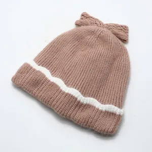 Détail d'un bonnet tricoté avec nœud rose et bordure ondulée blanche pour l'hiver