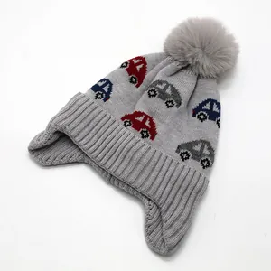 Close-up of children's grey knit beanie with plush pom-pom and car jacquard pattern