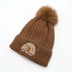 Detailed knit texture and embroidered cartoon animal on warm winter beanie with pom-pom