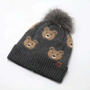 Detail of grey knitted kids beanie with bear patterns, pom-pom and leather logo tag
