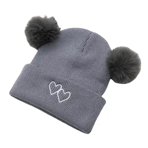 Detail of grey knitted baby hat with dual faux fur pom-poms and white heart embroidery