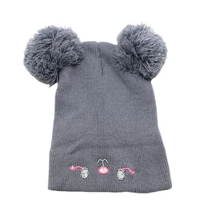 Detail of gray knitted infant hat with dual pom-poms and cute animal face embroidery