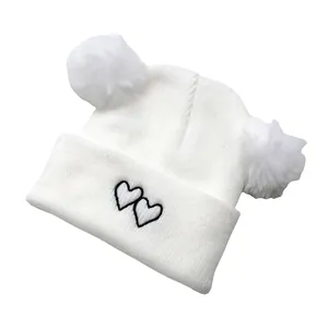 Close-up of white knit baby hat with soft faux fur pom-poms and black heart embroidery