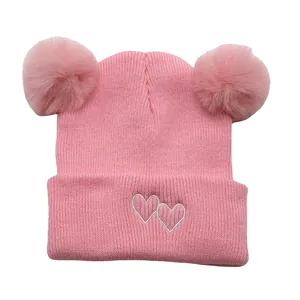 Pink knit baby beanie with double faux fur pom-poms and white heart embroidery