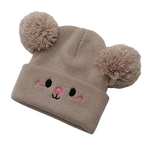 Detail of khaki knit hat featuring fluffy pom-poms and cute animal face embroidery