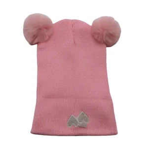 Detail of pink knitted baby hat with two faux fur pom-poms and gray heart embroidery