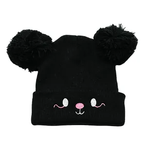 Detail of black knit kids hat featuring dual faux fur pom-poms and cartoon embroidery
