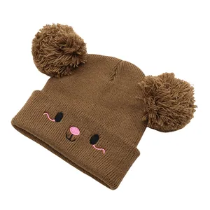Detail of a brown knit bear beanie featuring dual faux fur pom-poms and embroidered face