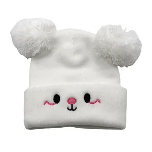 Close-up of white baby knit hat with fluffy pom-poms and cute embroidered animal face