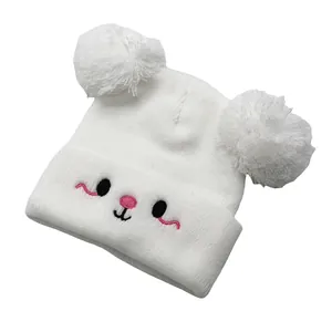 Detail of white knit baby hat with dual faux fur pom-poms and cute animal embroidery