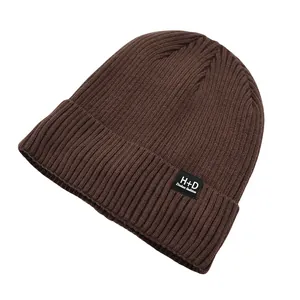 Détail du bonnet en maille côtelée marron foncé avec un écusson en tissu noir et blanc