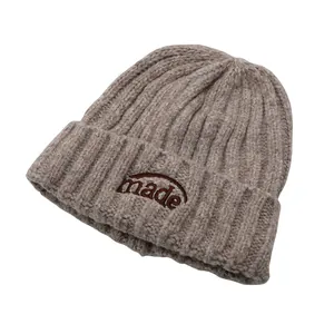 Nahaufnahme der dicken Rippstrick-Beanie mit braunem made-Stickmotiv in Beige-Melange