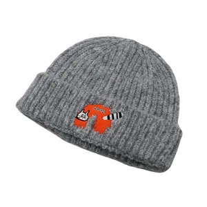Close-up of a grey knit beanie featuring a cute orange cat patch and COOL embroidery