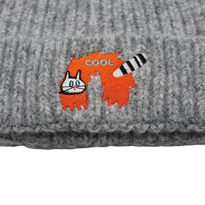Macro detail of high-quality embroidery featuring a white cat and COOL text on gray beanie