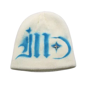 Detail showing knit texture of white beanie with blue graffiti and star stud