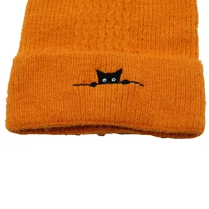 Detailed view of bright orange knit hat featuring cute black cat embroidery and soft texture